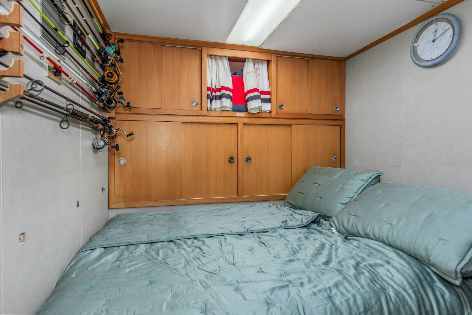 a bed with a blue sheet and a white pillow in a room with a clock and bookshel aboard BOSS Yacht for Sale
