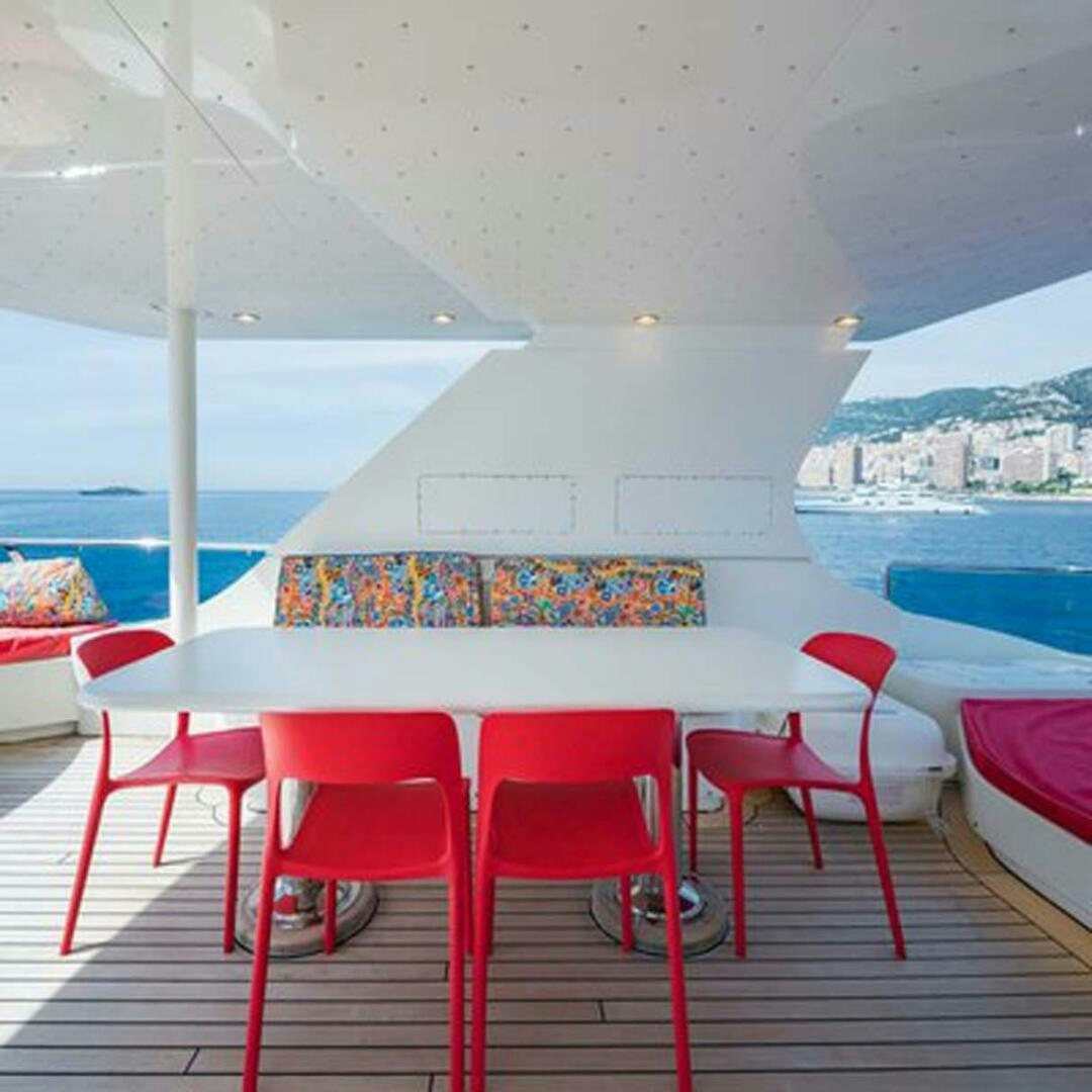 a table with red chairs on a deck with a city in the background aboard IRAMA Yacht for Sale