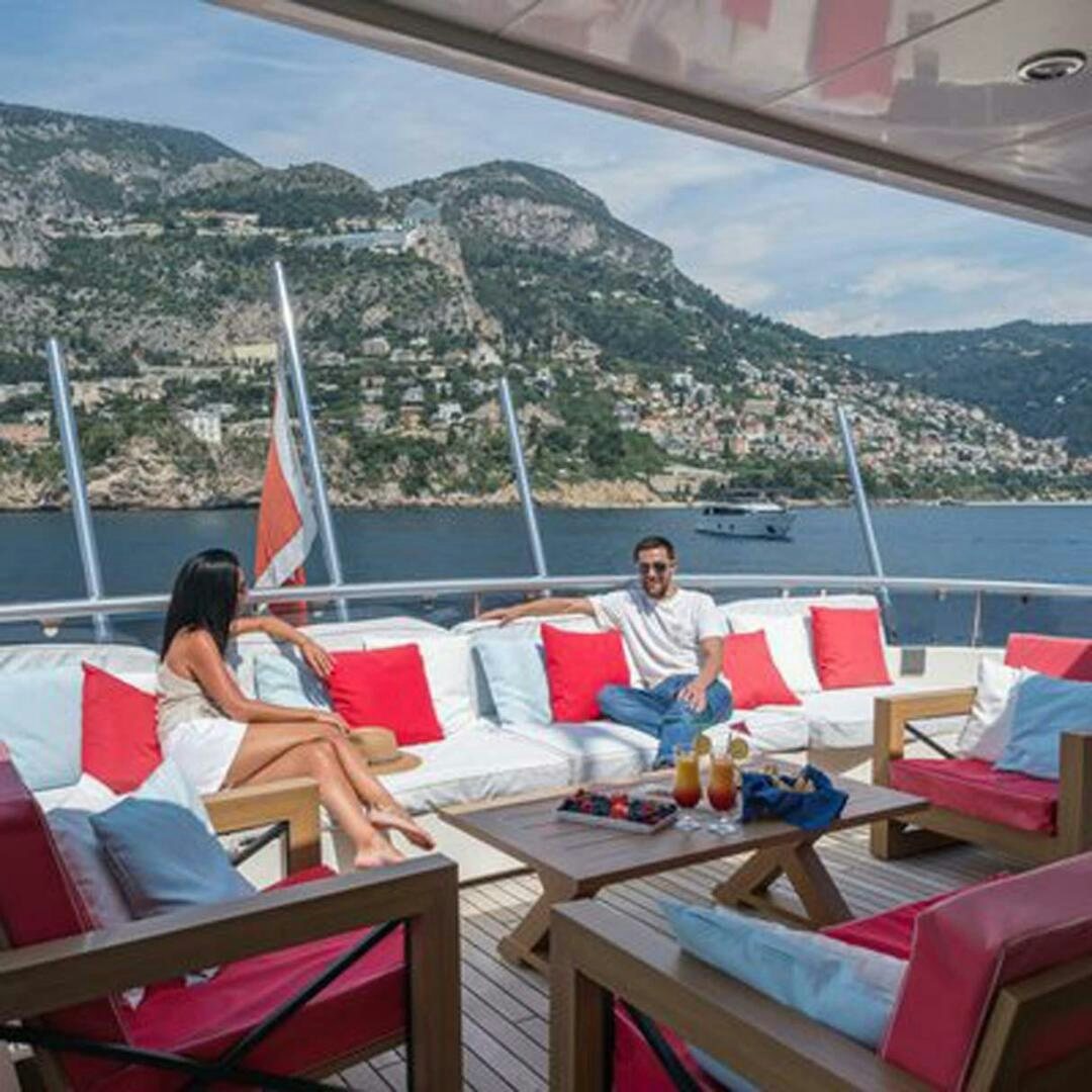 people sitting on lounge chairs on a beach with a sailboat in the background aboard IRAMA Yacht for Sale