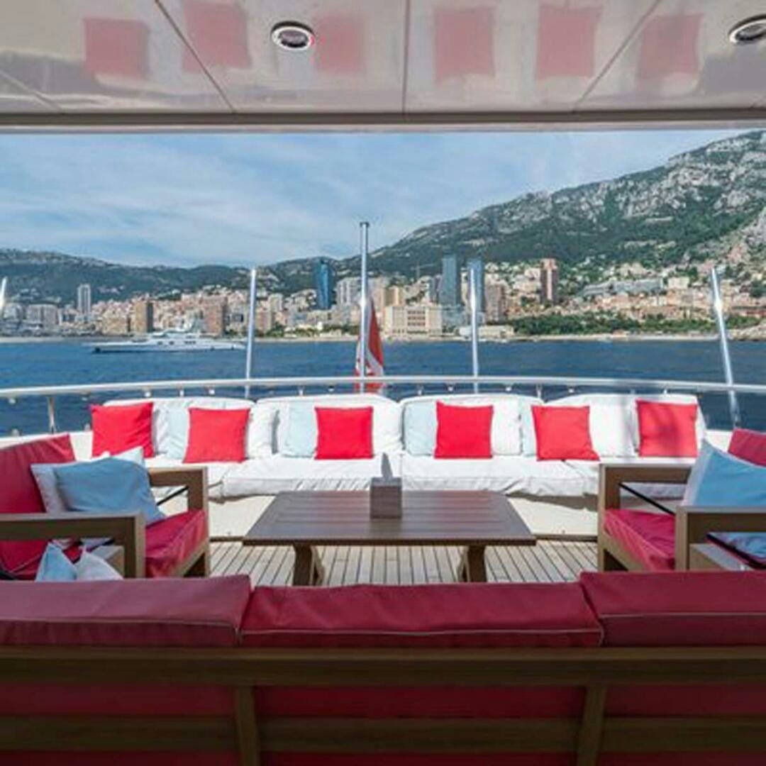 a group of red chairs on a beach with a city in the background aboard IRAMA Yacht for Sale