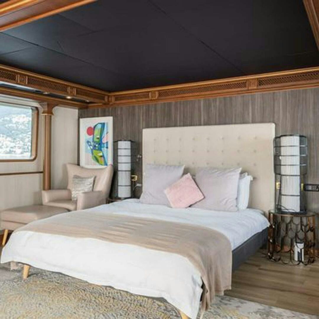 a bed with a white sheet and pillows in a room with a window aboard IRAMA Yacht for Sale