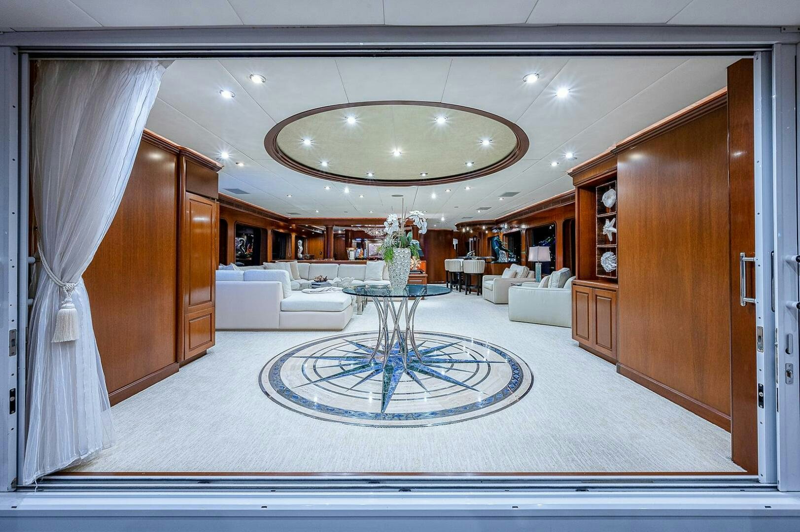 a large living room with a round table and a chandelier aboard LA SIRENA Yacht for Sale