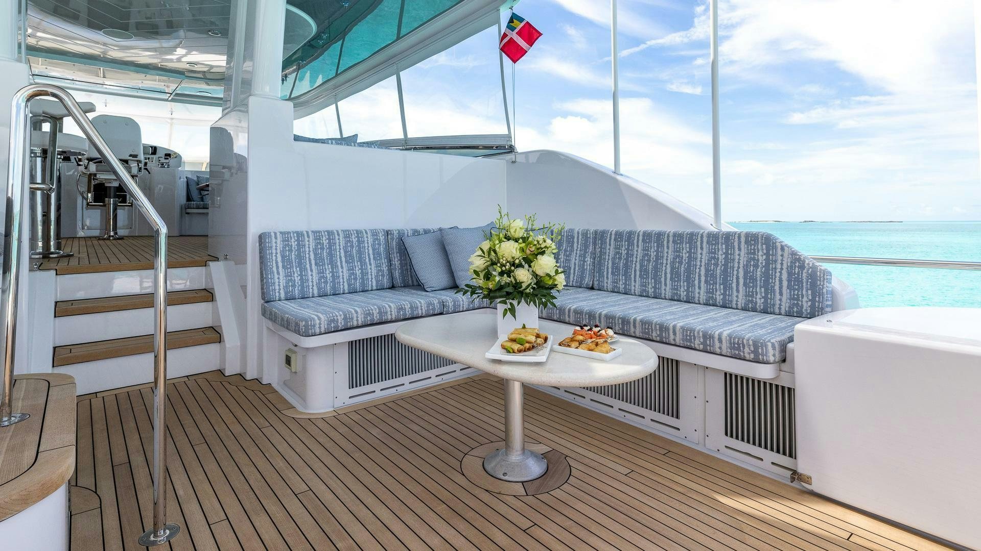 a white couch and a table on a balcony overlooking the ocean aboard NO SHORTCUTS Yacht for Sale