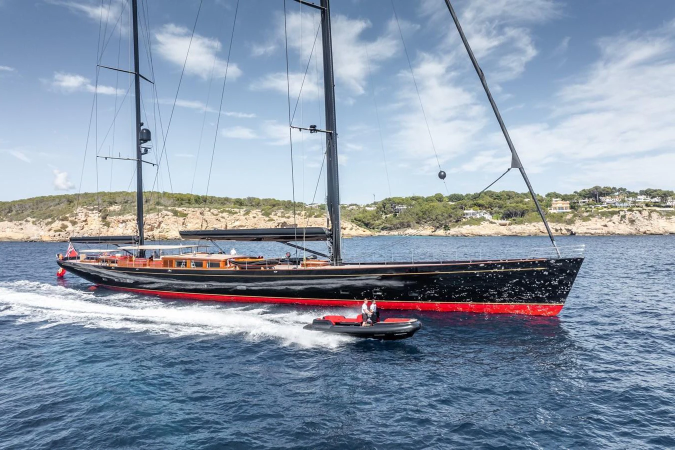 A sleek sailing yacht glides through the water, accompanied by a tender. aboard MAXIMUS Yacht for Sale