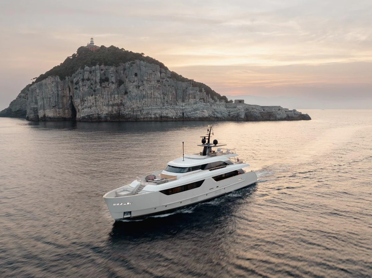 A sleek yacht cruises gracefully past a rugged island at sunset. aboard LET IT BE Yacht for Sale