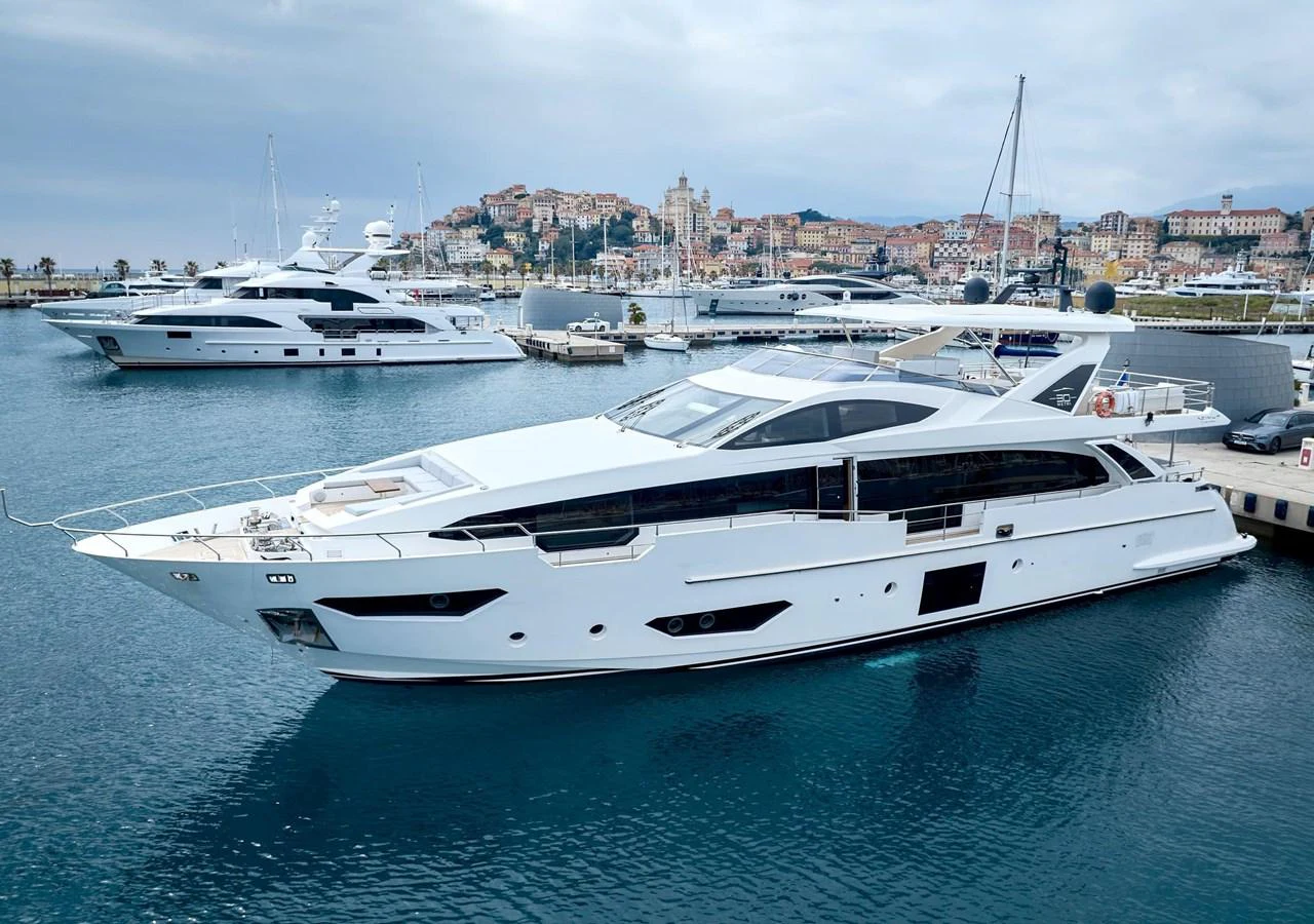 A sleek and modern yacht is docked in a picturesque marina with a charming coastal town in the background. aboard SUN & SEA Yacht for Sale