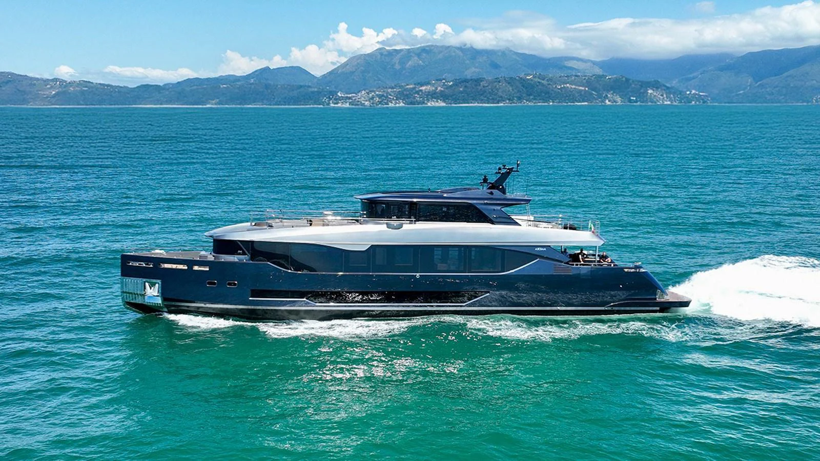 A sleek and modern yacht cruises through clear blue waters with a scenic mountainous backdrop. aboard LADY BETTY Yacht for Sale