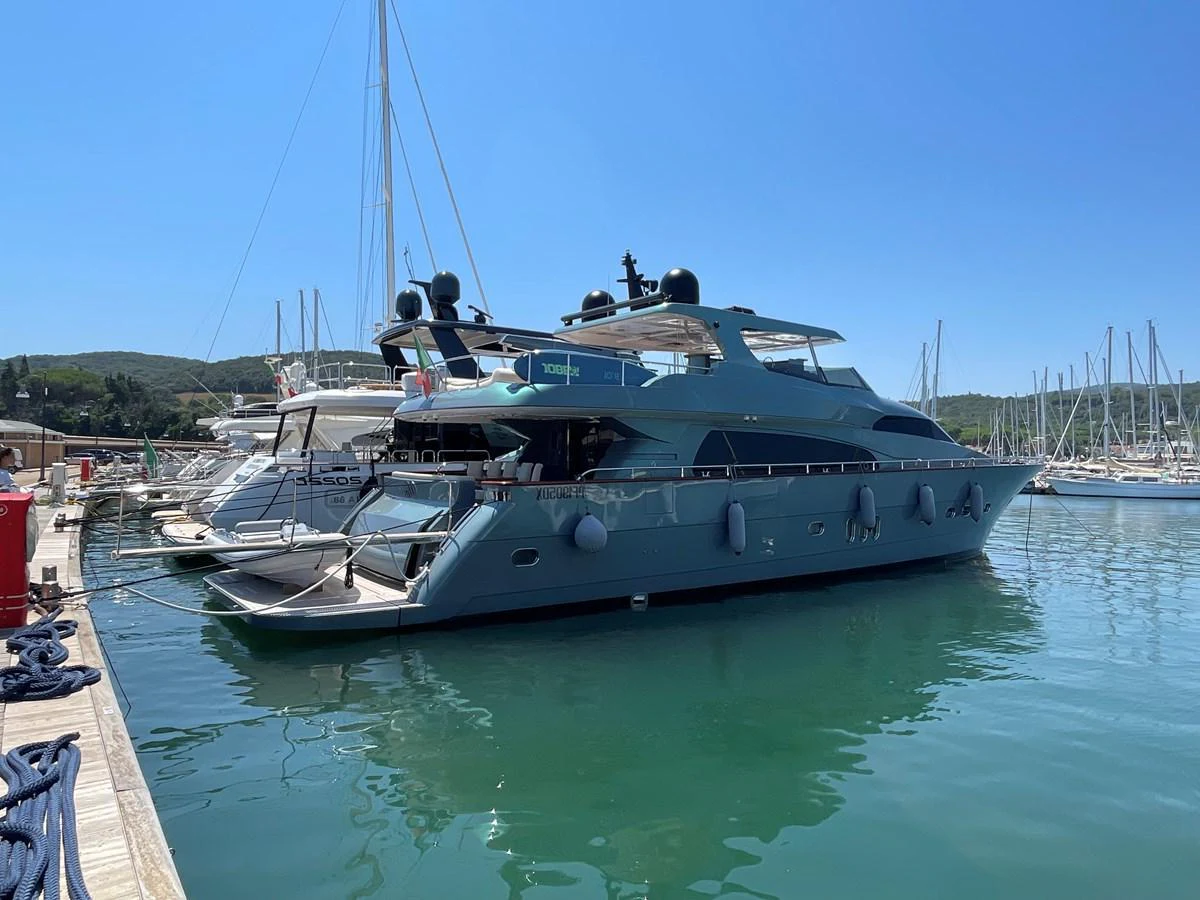A sleek and modern yacht docked in a serene marina under clear blue skies. aboard UNICA Yacht for Sale