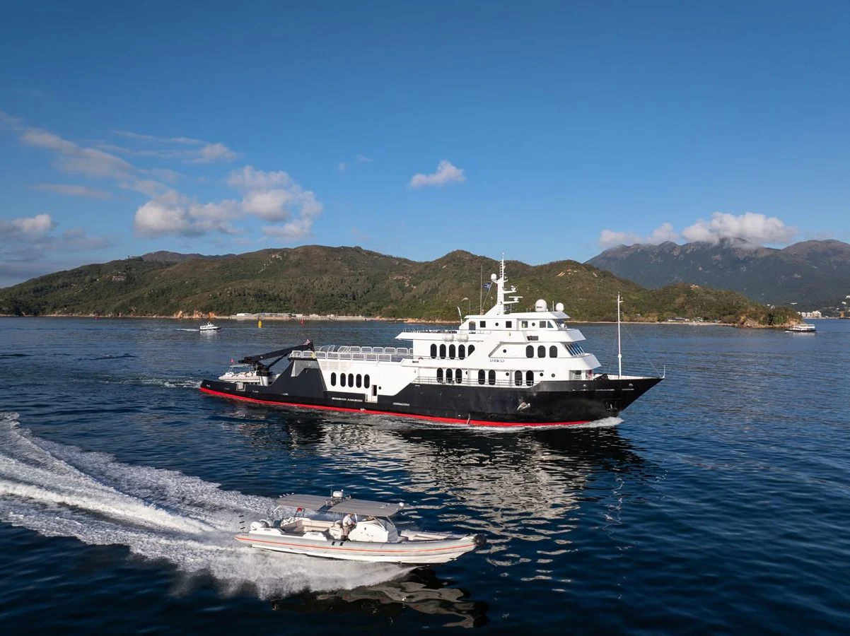 A sleek yacht cruises through calm waters with a scenic mountainous backdrop. aboard GLOBAL Yacht for Sale