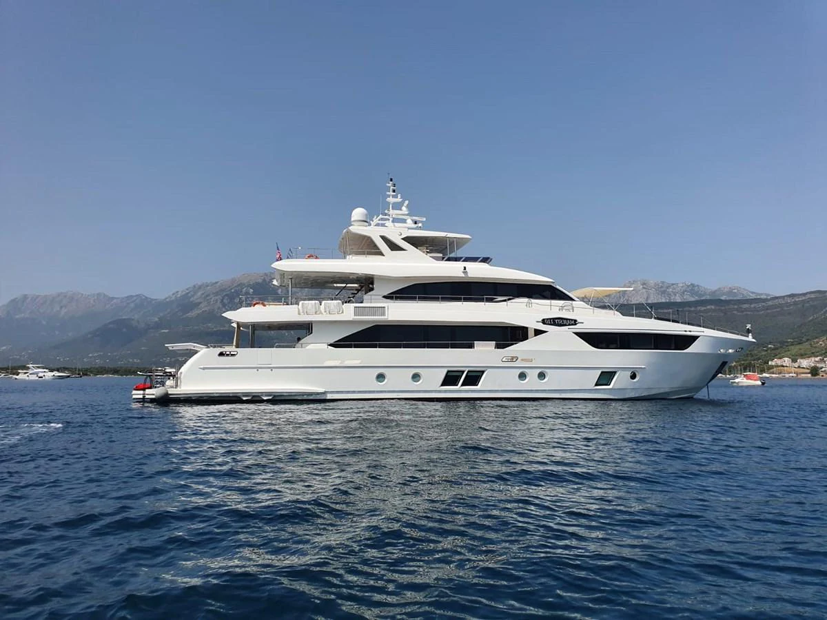 A luxurious yacht is anchored on calm blue waters with a scenic mountainous backdrop. aboard AMORE Yacht for Sale