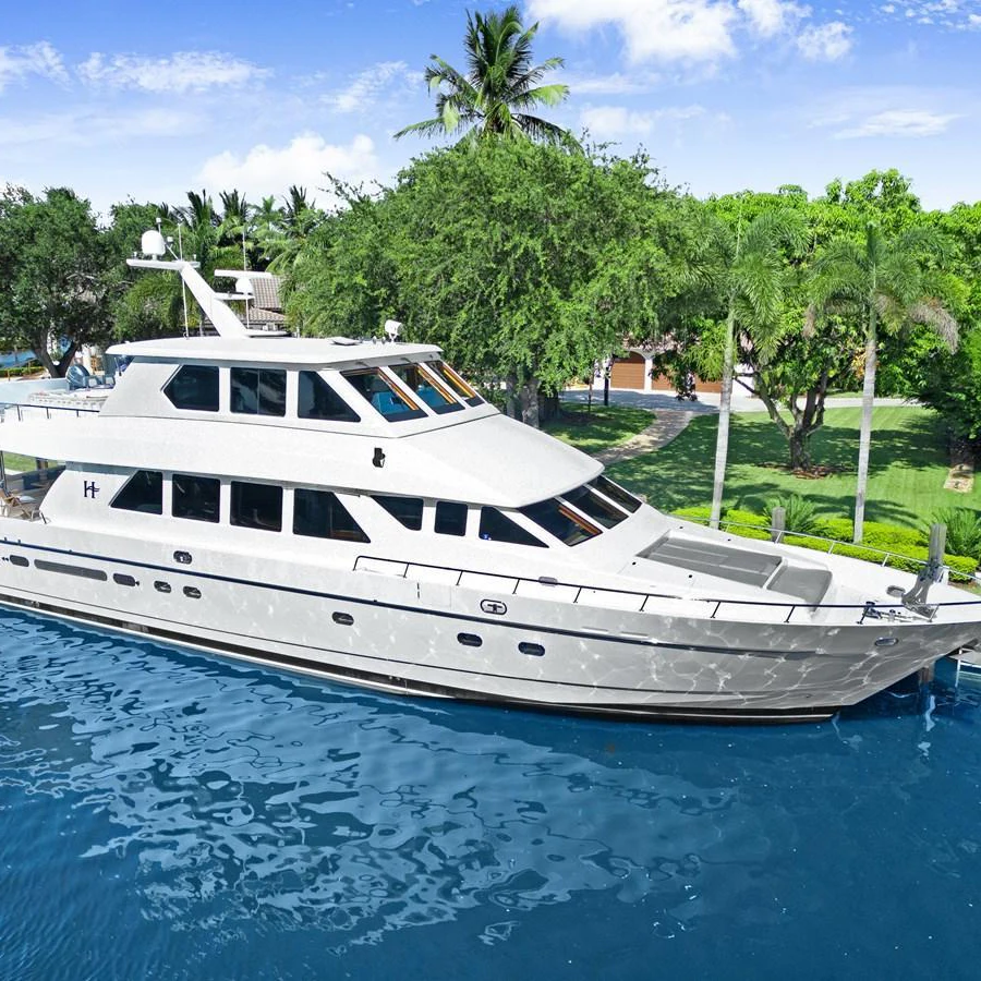 A sleek and elegant yacht is docked in a serene, tropical setting with lush greenery and clear blue water. aboard MILES AWEIGH Yacht for Sale