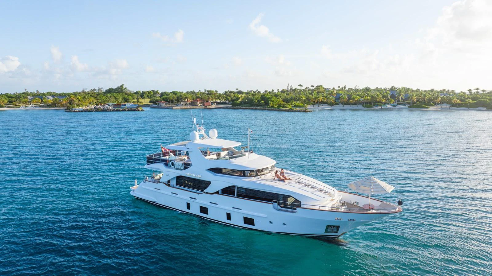 A luxurious yacht cruises serenely in clear blue waters near a lush, tropical shoreline. aboard SEA GYPSY Yacht for Sale