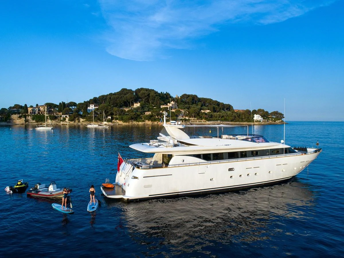 A sleek yacht is anchored in calm waters with a scenic coastal backdrop. aboard TALILA Yacht for Sale