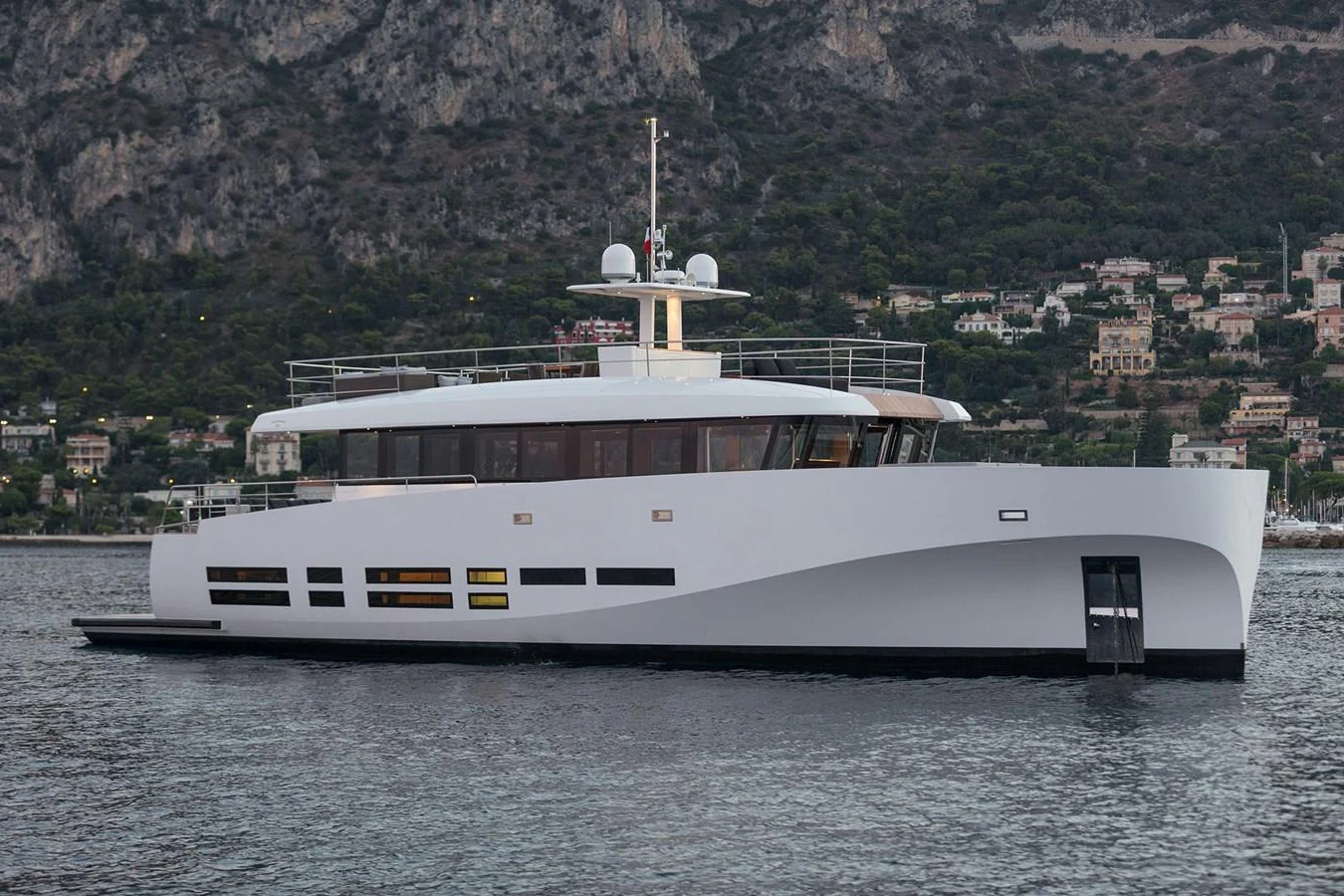 A sleek, modern yacht is anchored in calm waters with a scenic mountainous backdrop. aboard CASA Yacht for Sale