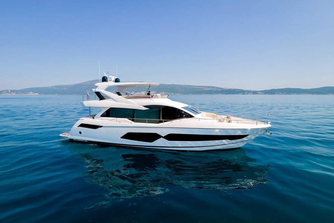 A sleek and modern yacht glides gracefully on calm blue waters under a clear sky. aboard SUNSEEKER 76Y Yacht for Sale