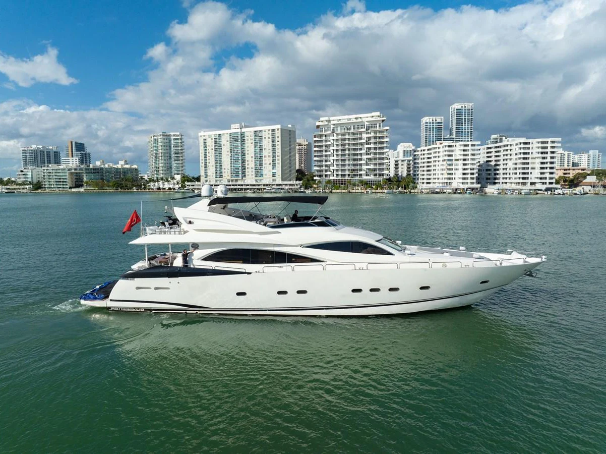 A sleek, modern yacht cruises gracefully on calm waters with a cityscape in the background. aboard SO WHAT WHO CARES Yacht for Sale