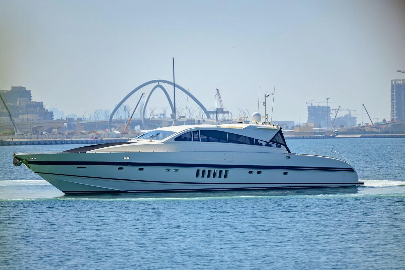 A sleek and modern yacht glides gracefully through calm waters with a cityscape in the background. aboard SEA SQUIRTER Yacht for Sale