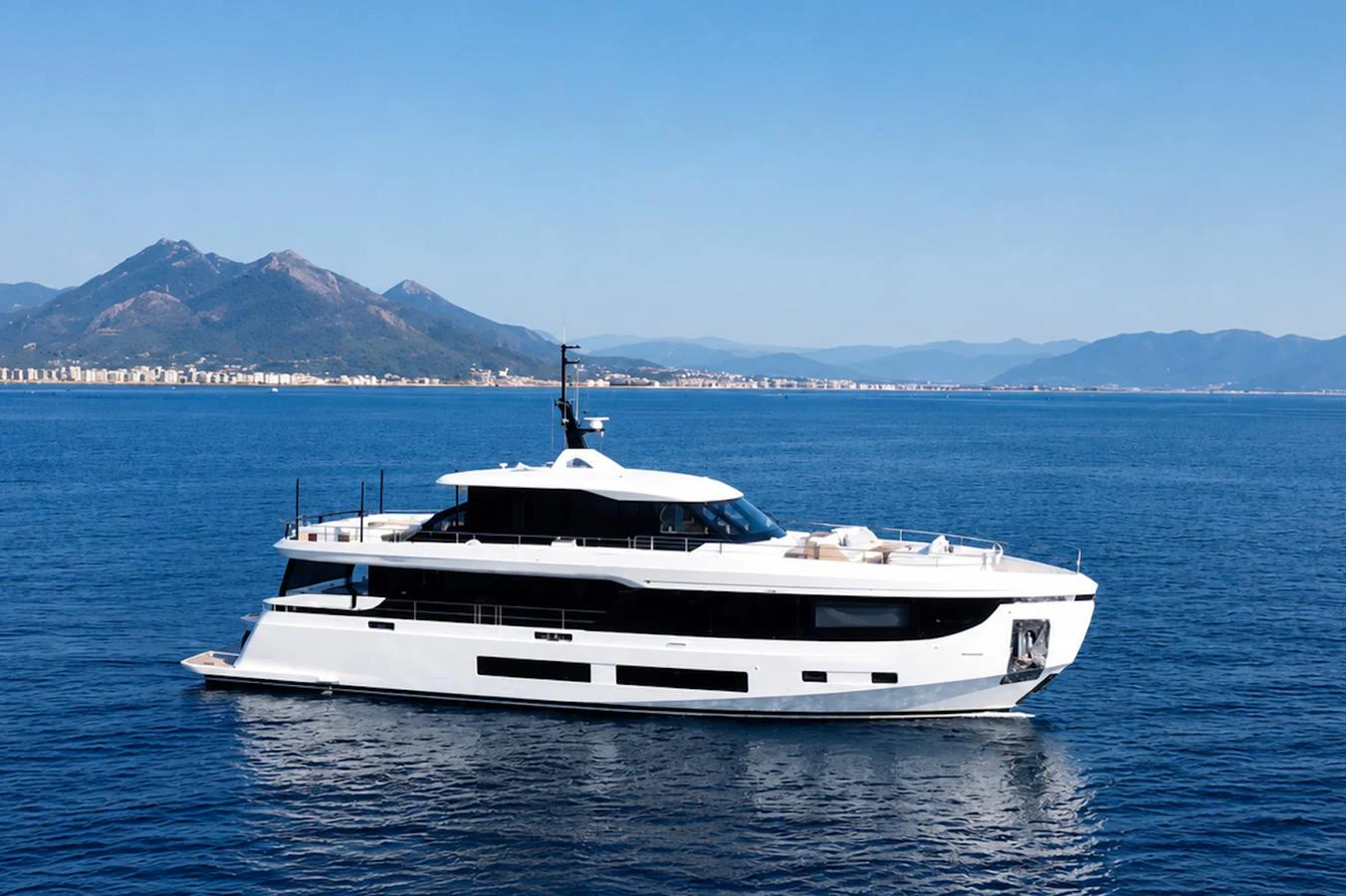 A sleek and modern yacht cruising on calm blue waters with a mountainous backdrop. aboard COME TOGETHER Yacht for Sale