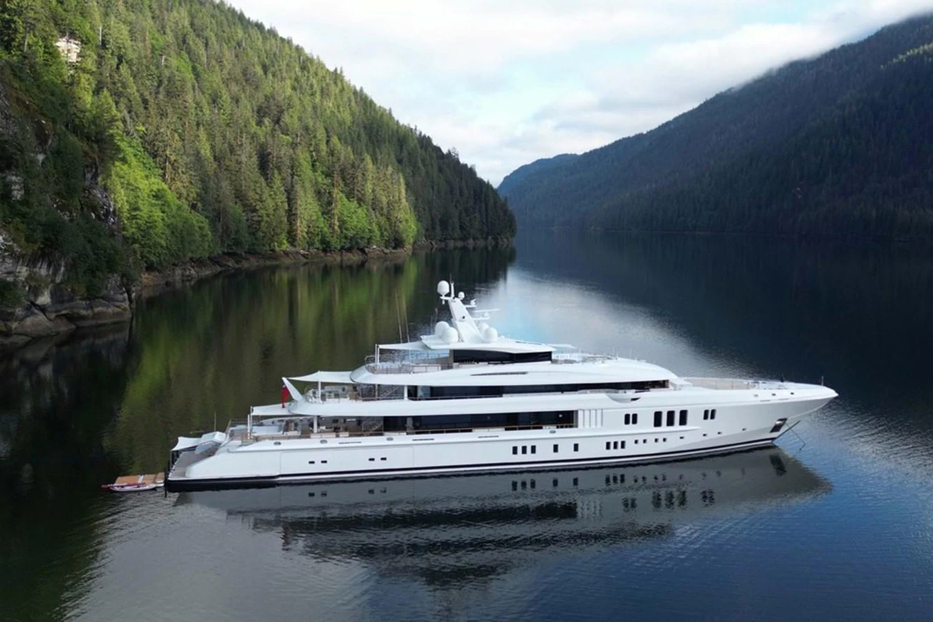 A sleek and modern yacht glides gracefully through a serene, forest-lined waterway. aboard DYTAN Yacht for Sale