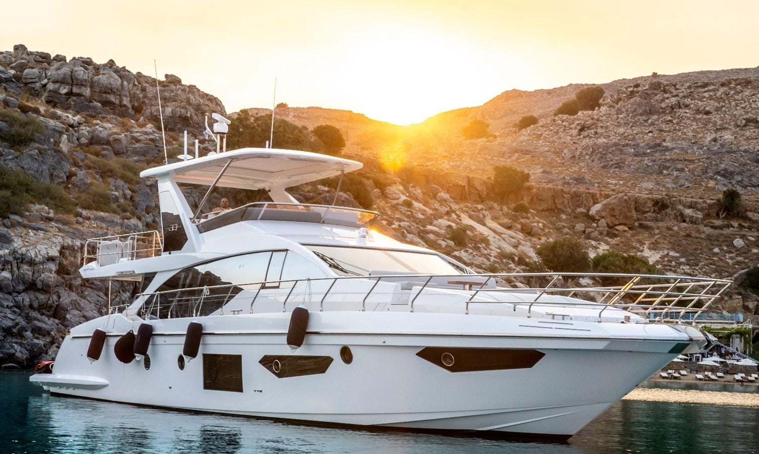 a white boat on a body of water with a hill in the background aboard ATLANTIS OF LONDON Yacht for Sale