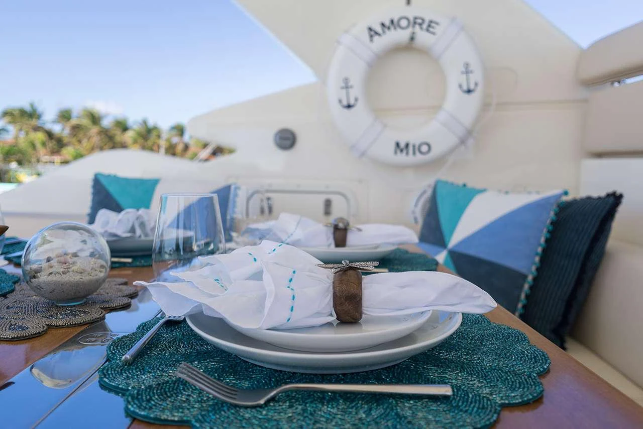 A beautifully set dining table on the yacht, featuring elegant tableware and a decorative lifebuoy in the background. aboard LA MAR Yacht for Charter