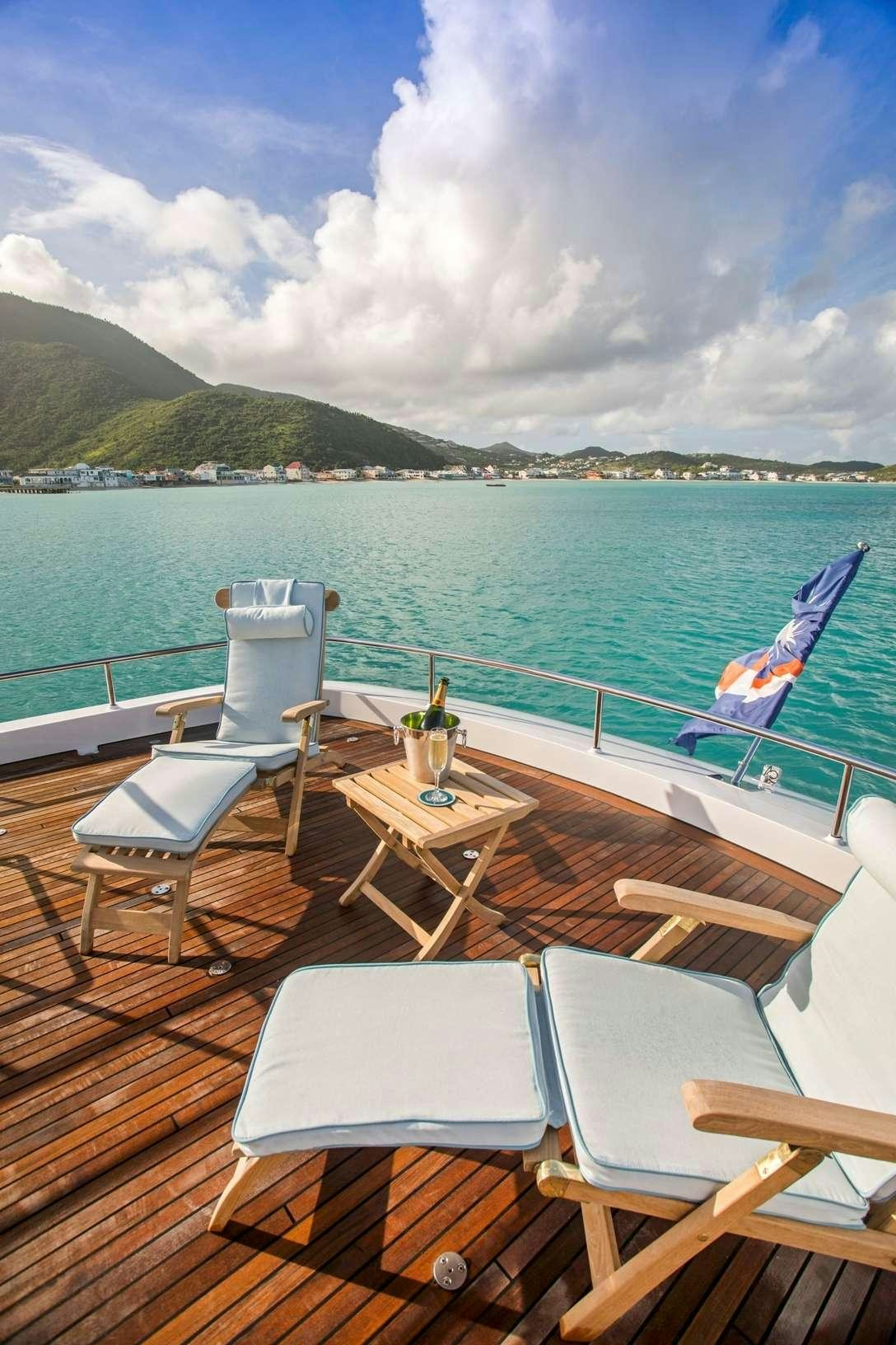 a deck with chairs and tables on it by a body of water aboard PURA VIDA Yacht for Charter