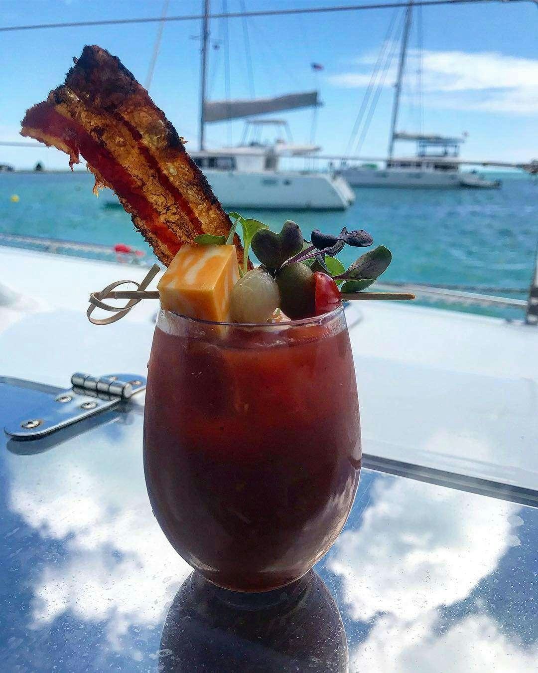 a glass with a drink and fruit on a table with a boat in the background aboard SANTA ANA Yacht for Charter