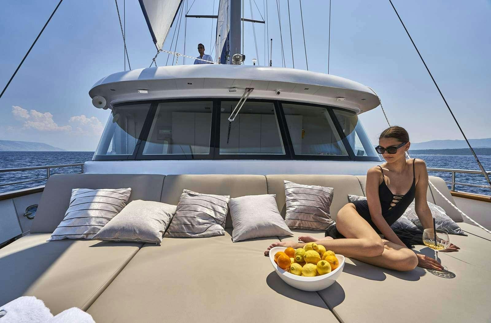 a person sitting on a couch on a boat with a bowl of fruit aboard DALMATINO Yacht for Charter
