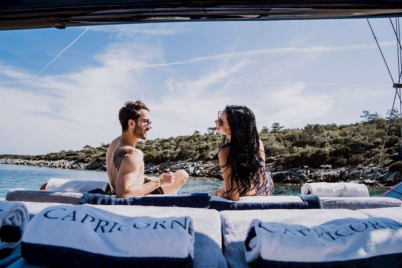 a man and woman sitting on a lounge chair on a beach aboard CAPRICORN 1 Yacht for Charter