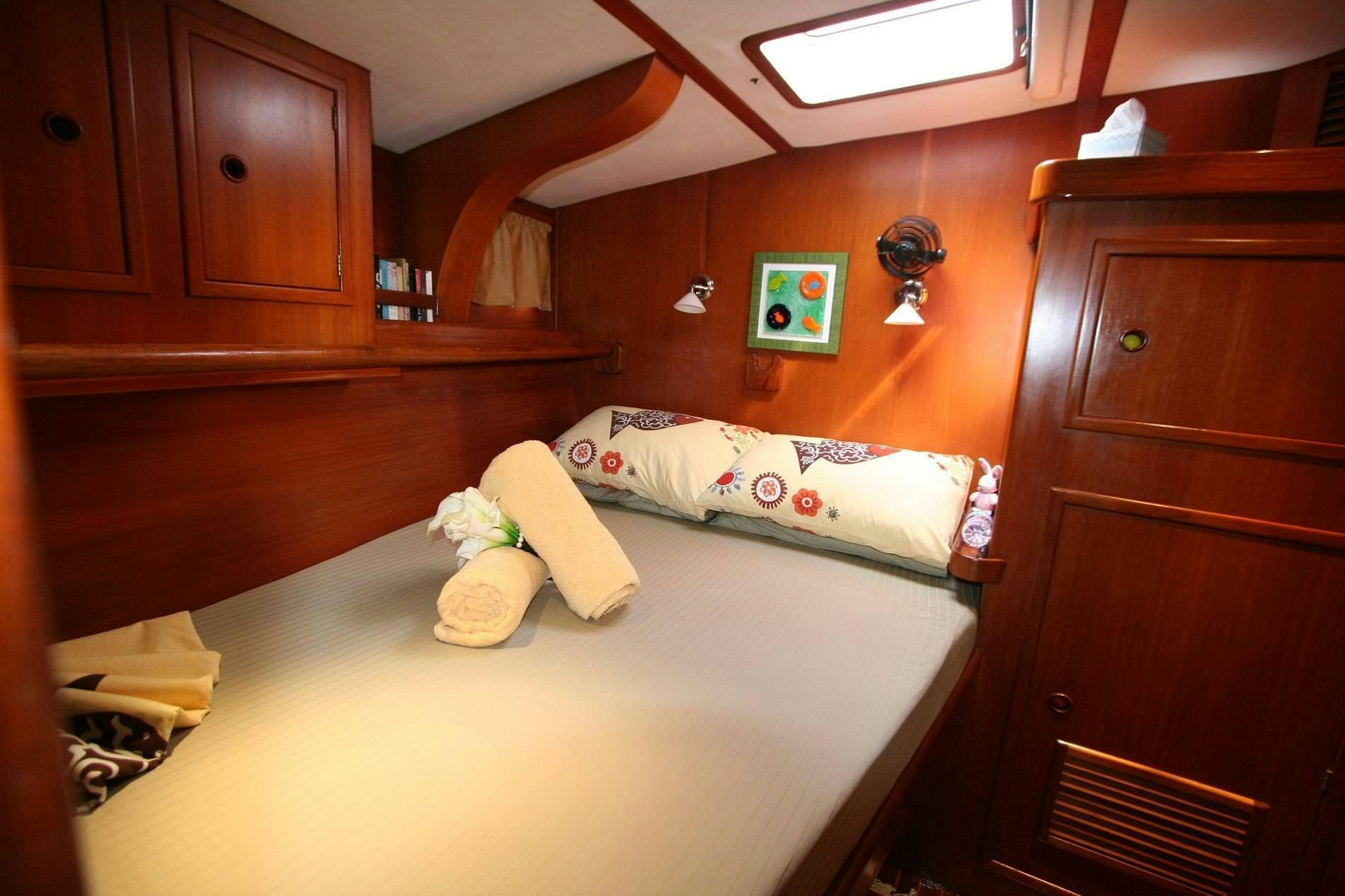 a bed with a white sheet and pillows in a room with wood cabinets aboard ANAHITA Yacht for Charter