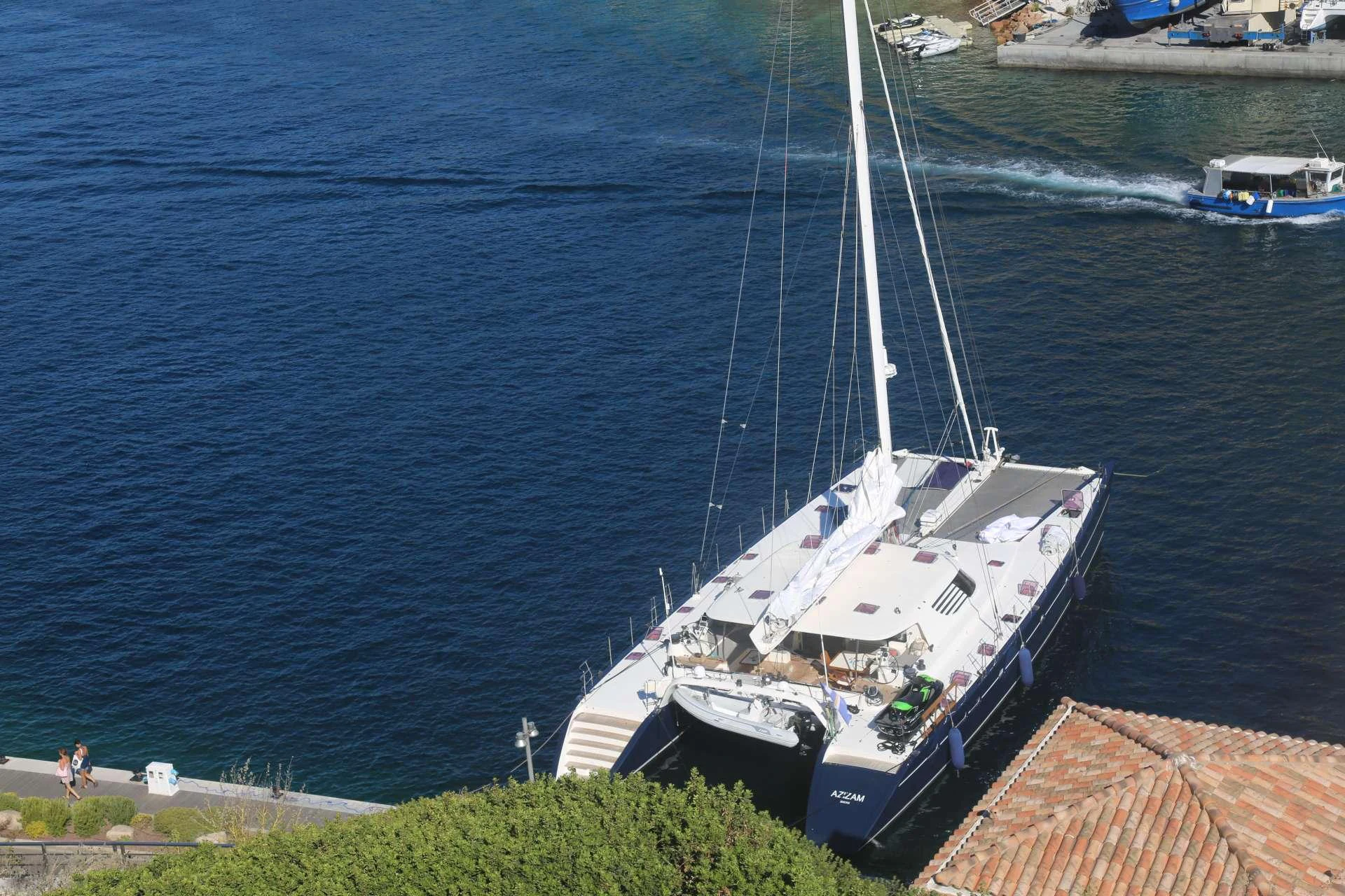 A luxurious catamaran is docked in a serene marina, showcasing its sleek design and spacious deck. aboard AZIZAM Yacht for Charter