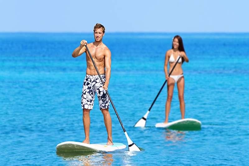 a man and woman on paddle boards in the ocean aboard CHAMPAGNE Yacht for Charter