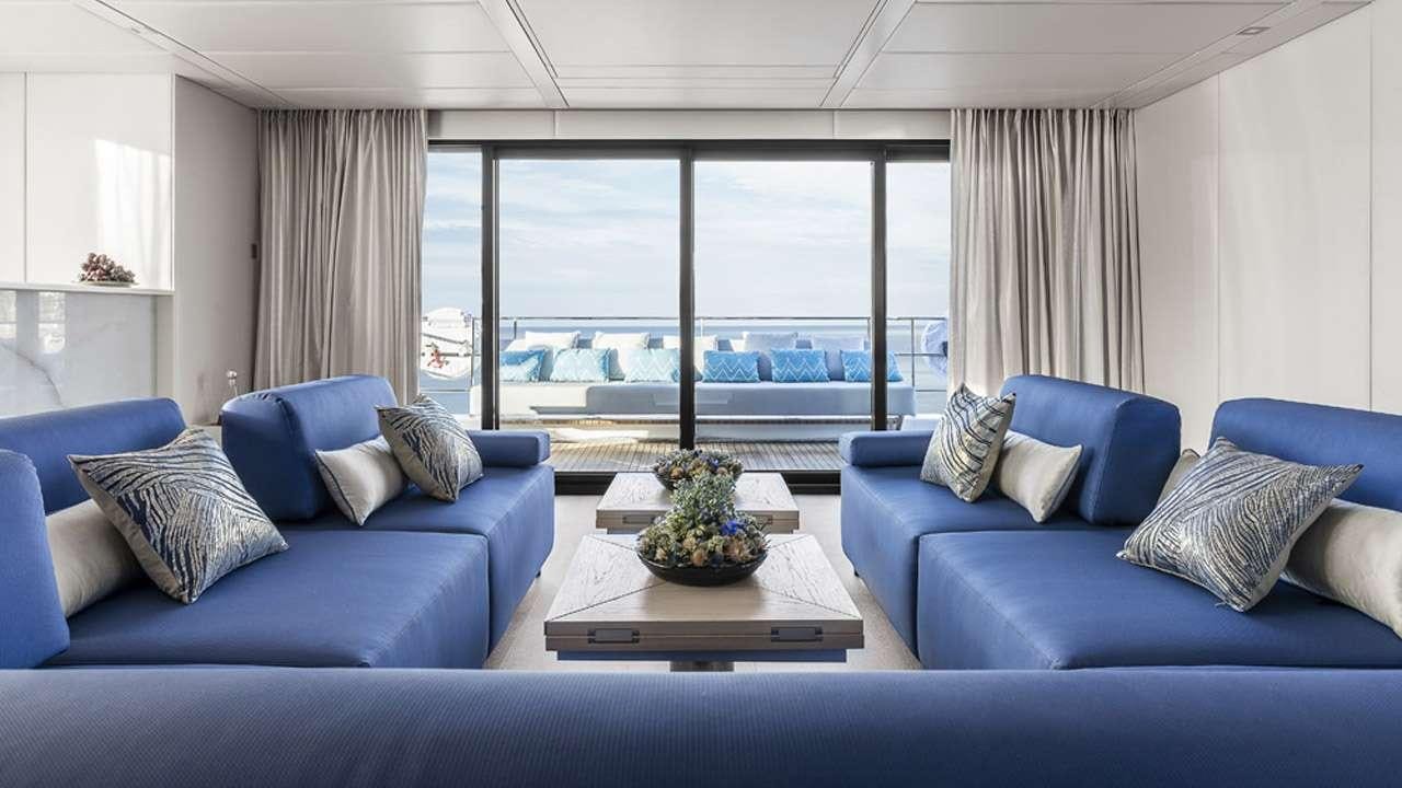 a living room with blue couches and a large window aboard MAYRILOU Yacht for Charter