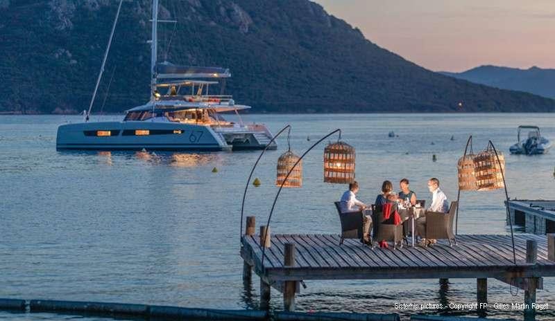 a group of people sitting on a dock with a boat in the water aboard BLACK CAT Yacht for Charter
