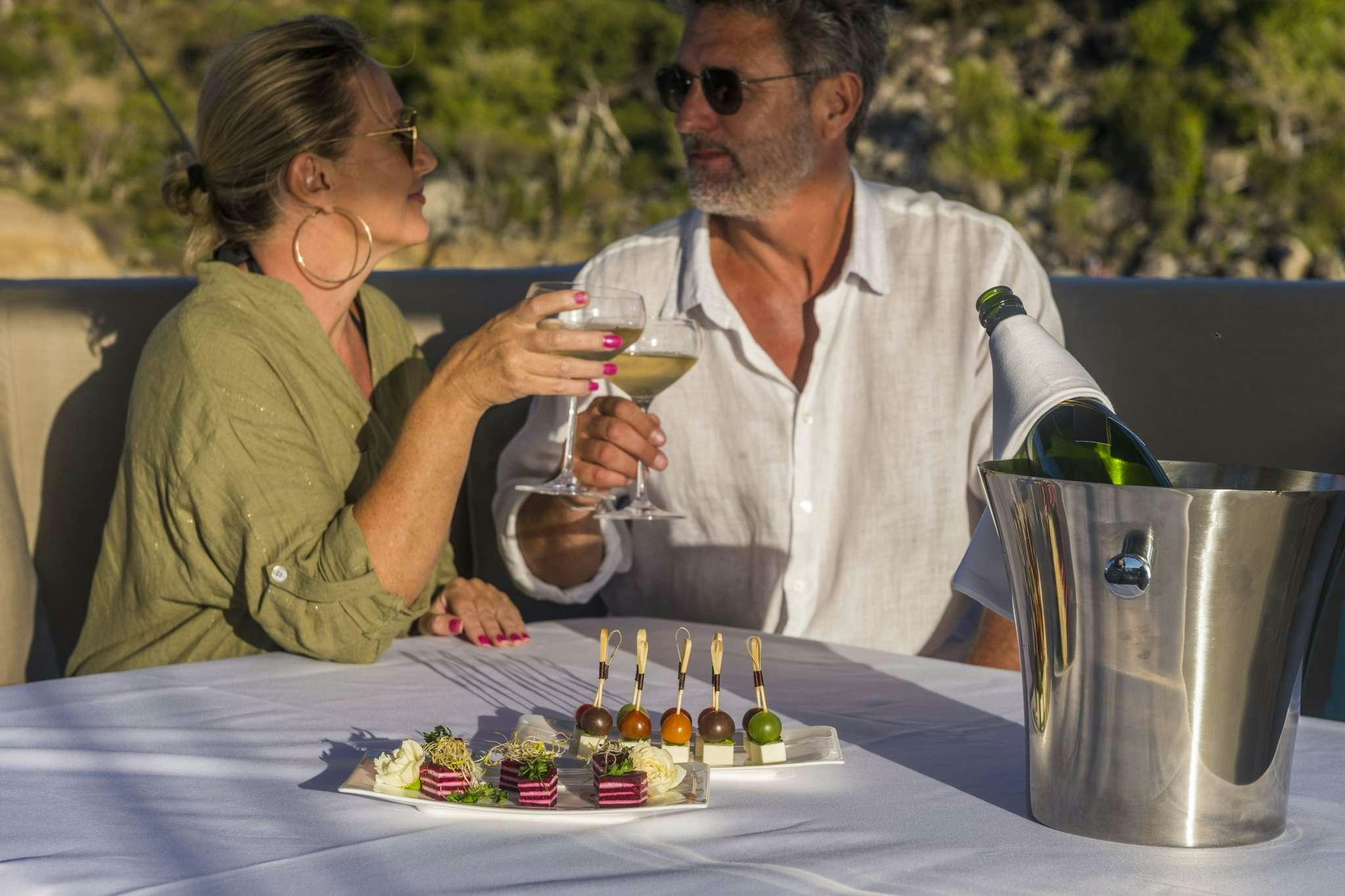 a man and a woman sitting at a table with a cake and drinks aboard LISA OF THE SEAS Yacht for Charter