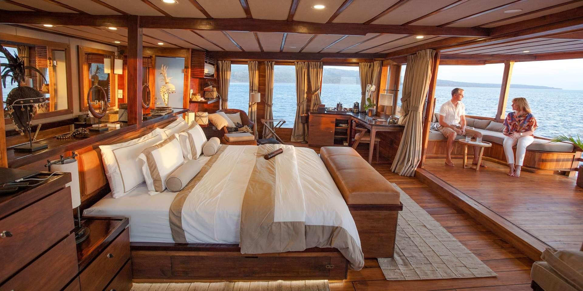 a couple of people sitting in a room with a bed and a table aboard PRANA Yacht for Charter