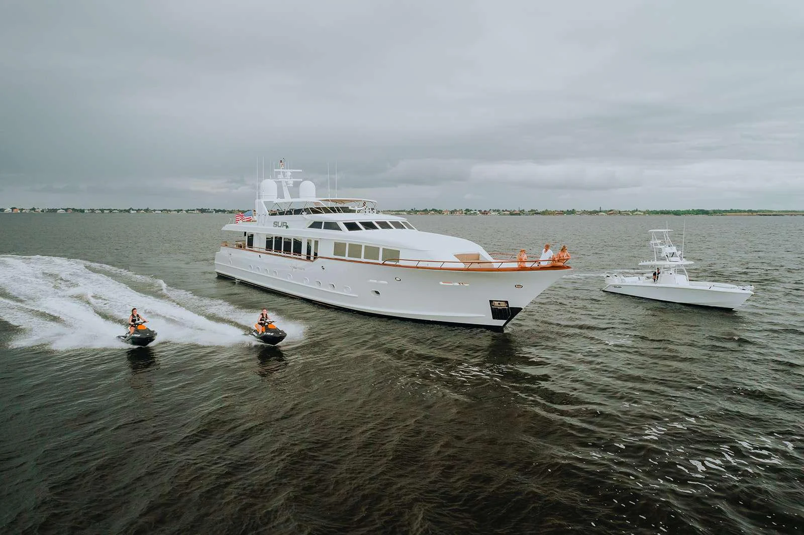 A luxurious yacht cruises through the water accompanied by two jet skis and a smaller boat. aboard SKY Yacht for Charter