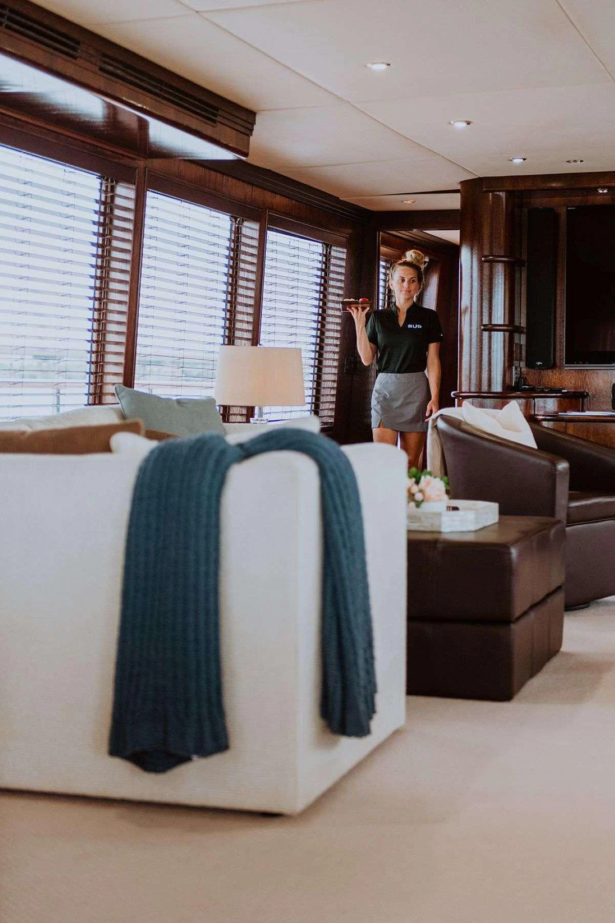 A cozy yacht interior with comfortable seating and a crew member standing in the background. aboard SKY Yacht for Charter