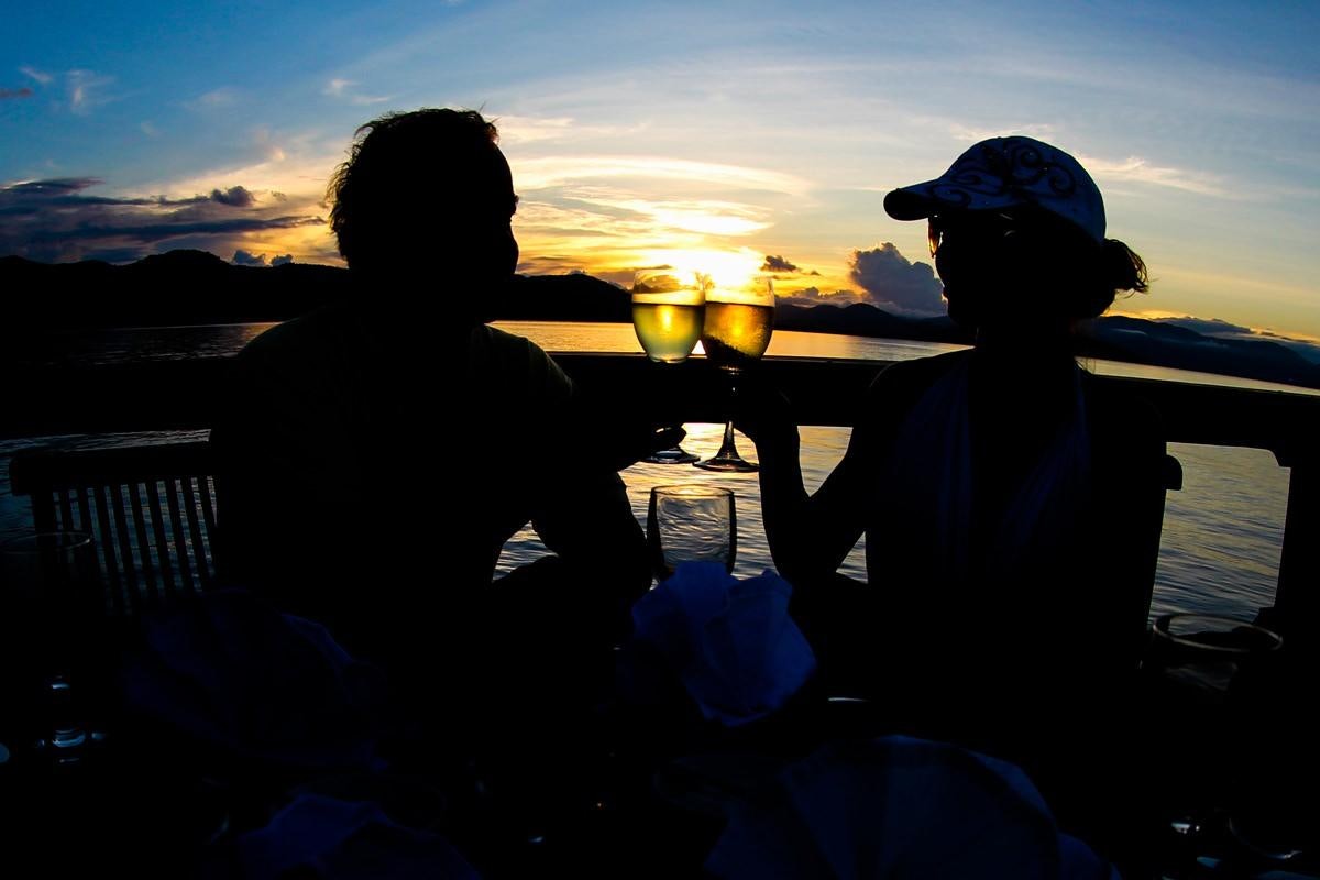 a couple of people sitting at a table with a sunset in the background aboard DAMAI Yacht for Charter