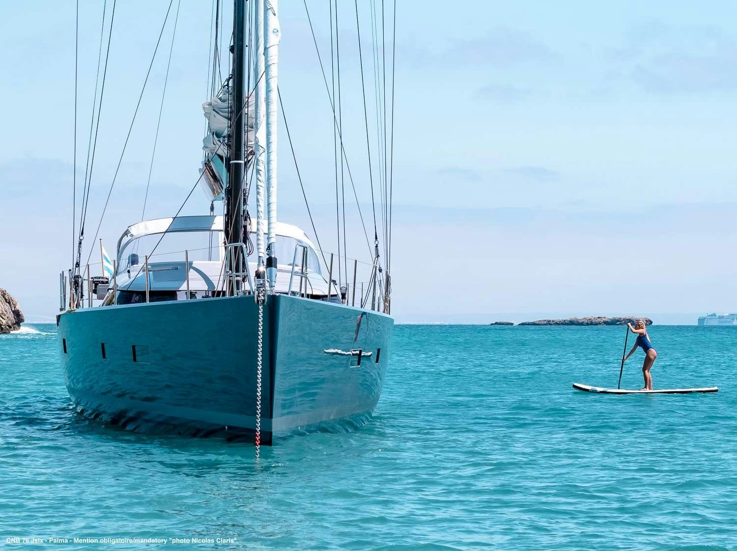 a person on a surfboard next to a sailboat aboard J SIX Yacht for Charter