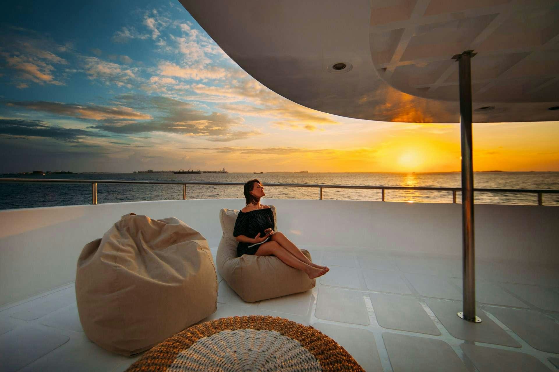 a person sitting on a chair on a rooftop with a sunset in the background aboard ALICE Yacht for Charter