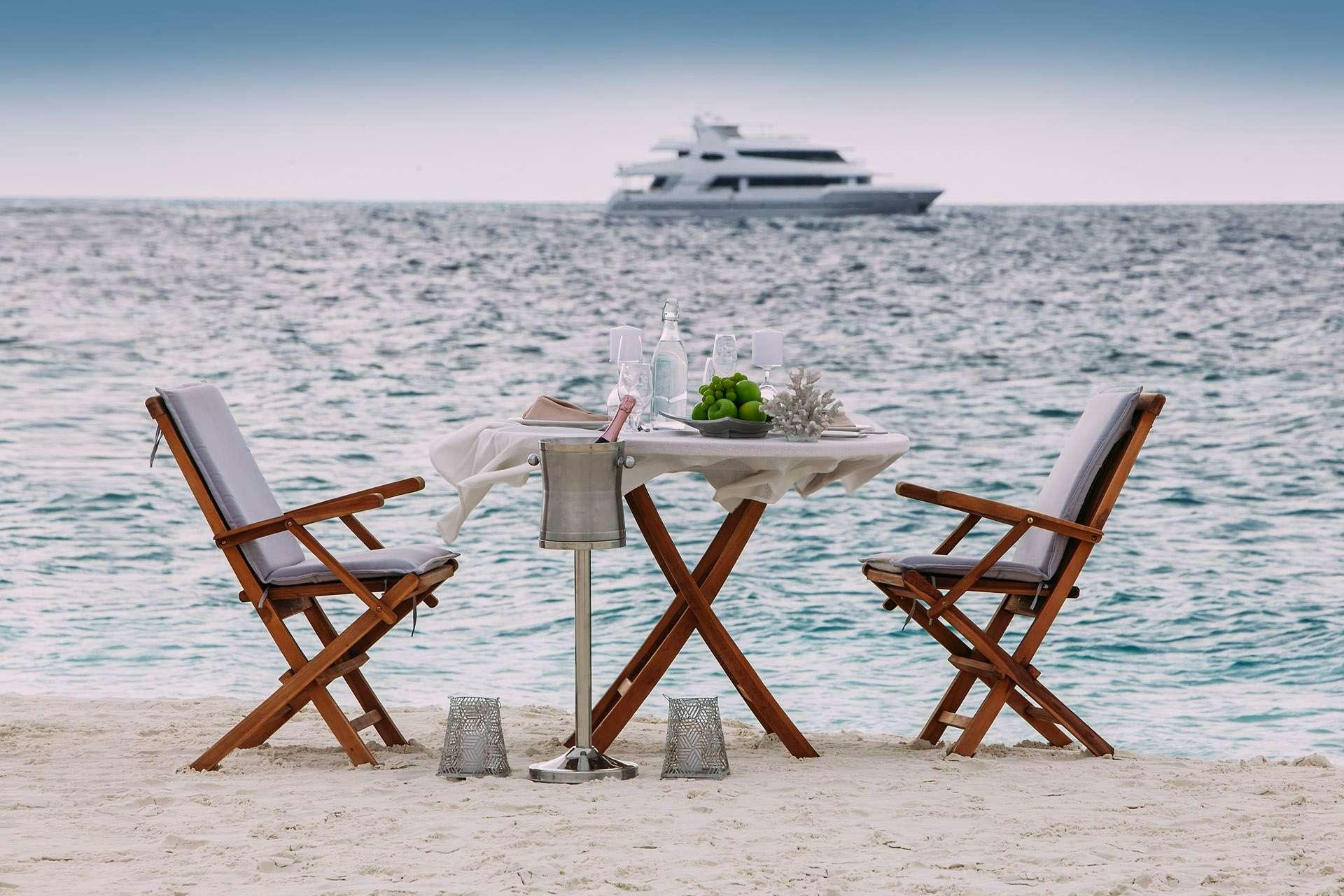 a couple of chairs and a table on a beach with a boat in the background aboard ALICE Yacht for Charter