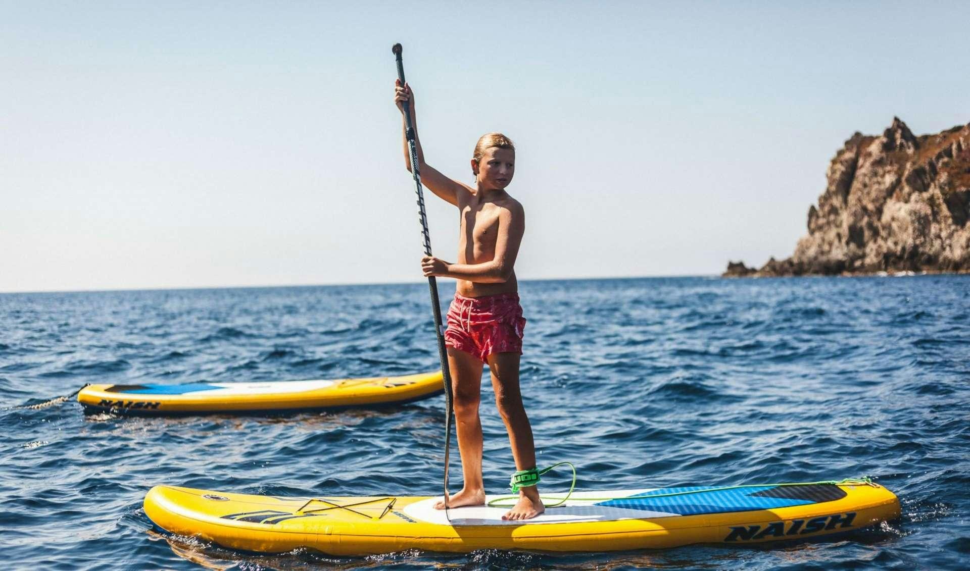 a boy standing on a paddle board aboard OCEAN VIEW Yacht for Charter