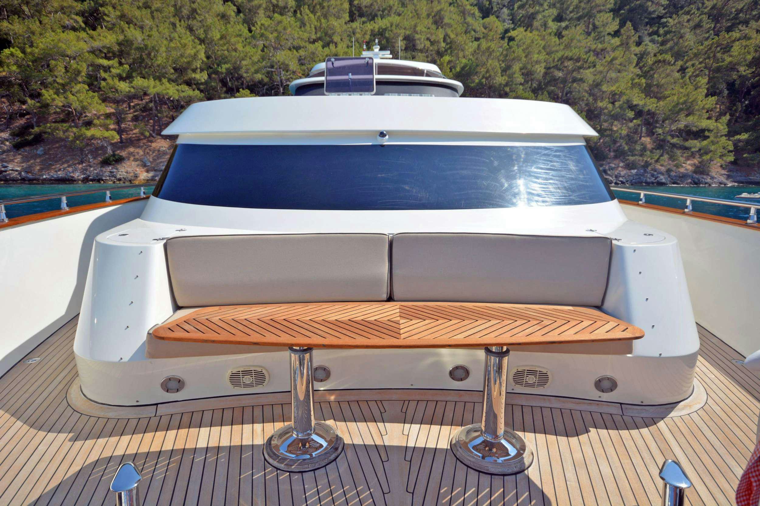 a white rectangular object with a wooden surface and a metal bar on a deck with trees in the aboard GO Yacht for Charter