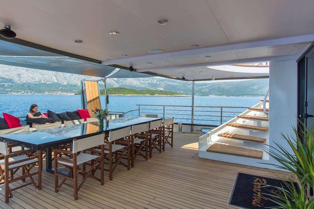 a person sitting at a table in a restaurant with a body of water in the background aboard RARA AVIS Yacht for Charter