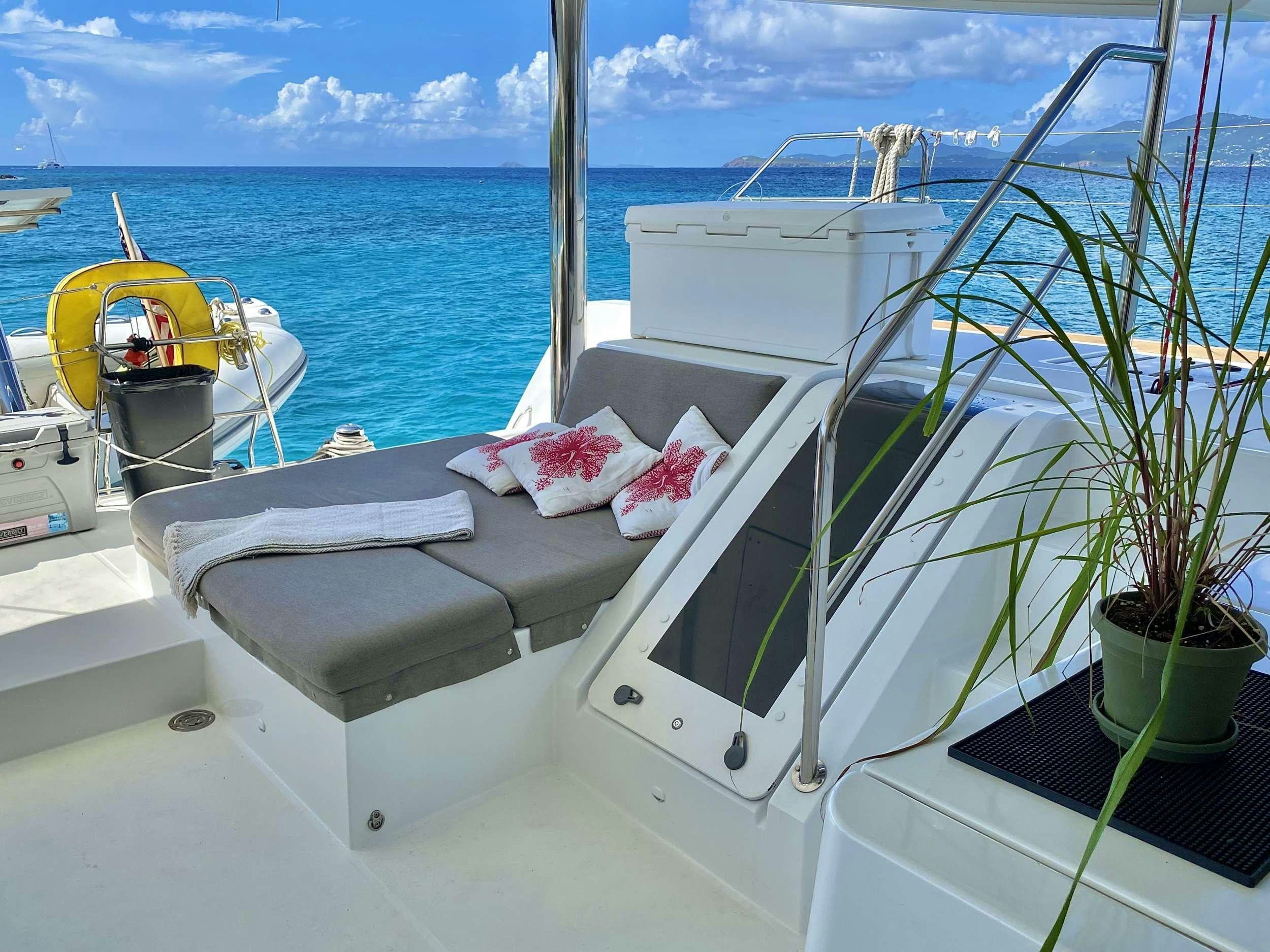 a white boat with pink pillows on a deck with a view of the ocean and blue sky aboard RUMBA Yacht for Charter