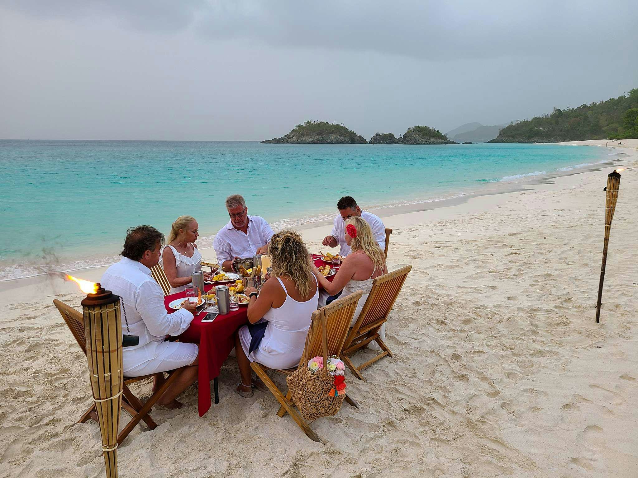 a group of people sitting around a table on a beach aboard CHAMPS ELYSEES Yacht for Charter