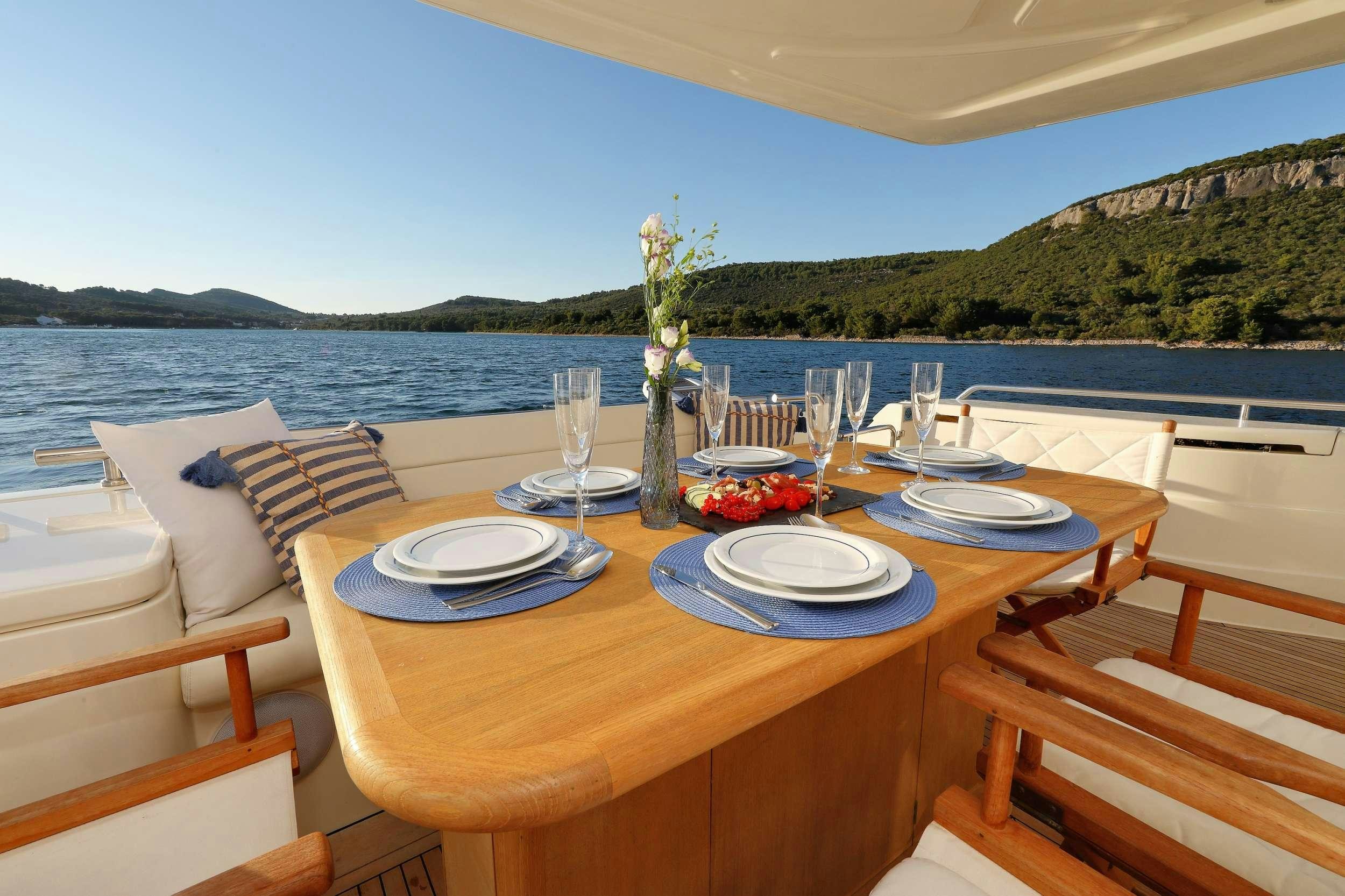 a table set with plates and glasses on a patio with a body of water and trees in the aboard dominique Yacht for Charter