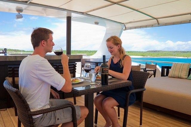 a man and woman sitting at a table with wine glasses and a bottle of wine on it aboard GALAPAGOS SEA STAR JOURNEY Yacht for Charter