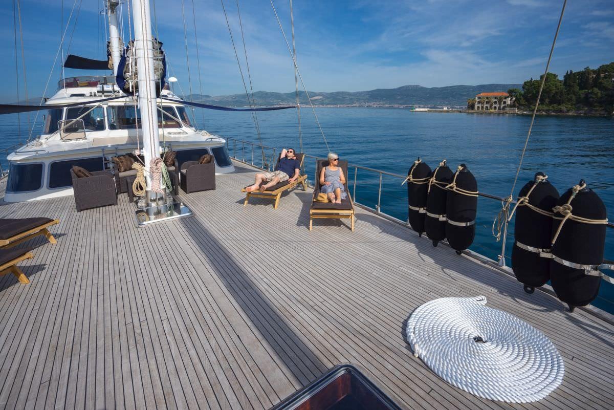 a person sitting on a chair on a dock next to a boat aboard ALBA Yacht for Charter
